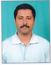 Portrait of a man with short black hair and a mustache, wearing a light blue collared shirt, against a turquoise background.